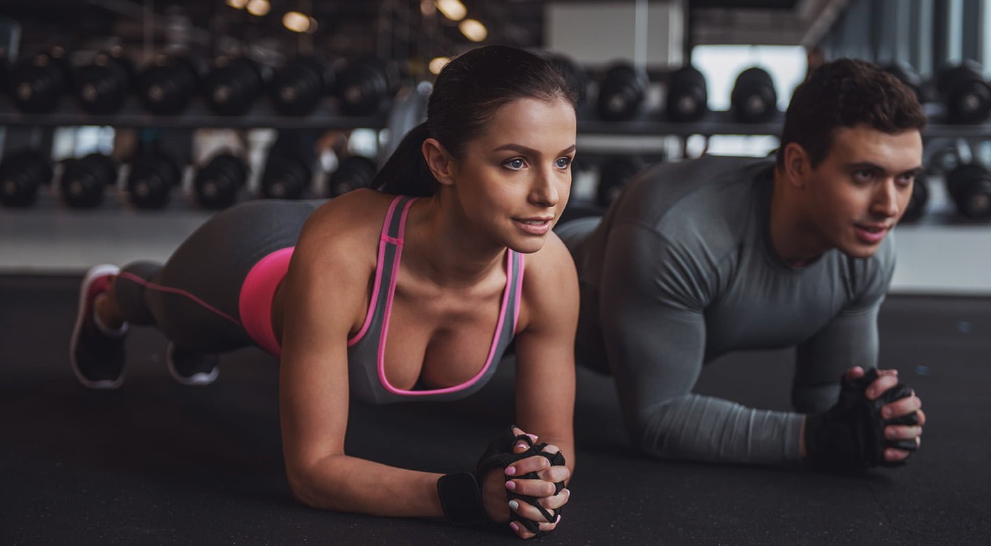 People in gym Attractive young muscular man and woman doing plank exercise while working out in gym